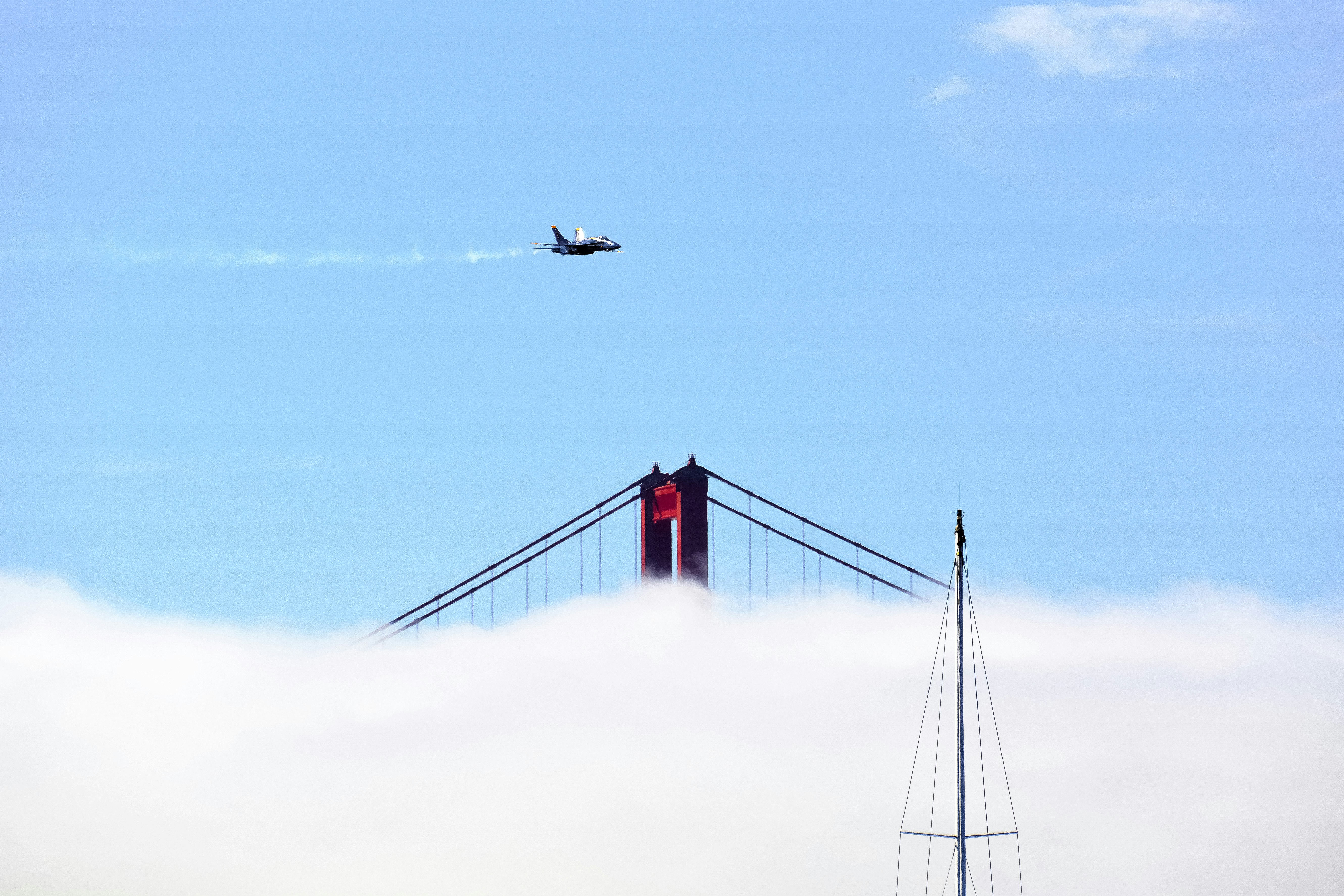 black and white airplane flying over red and white bridge under blue sky during daytime